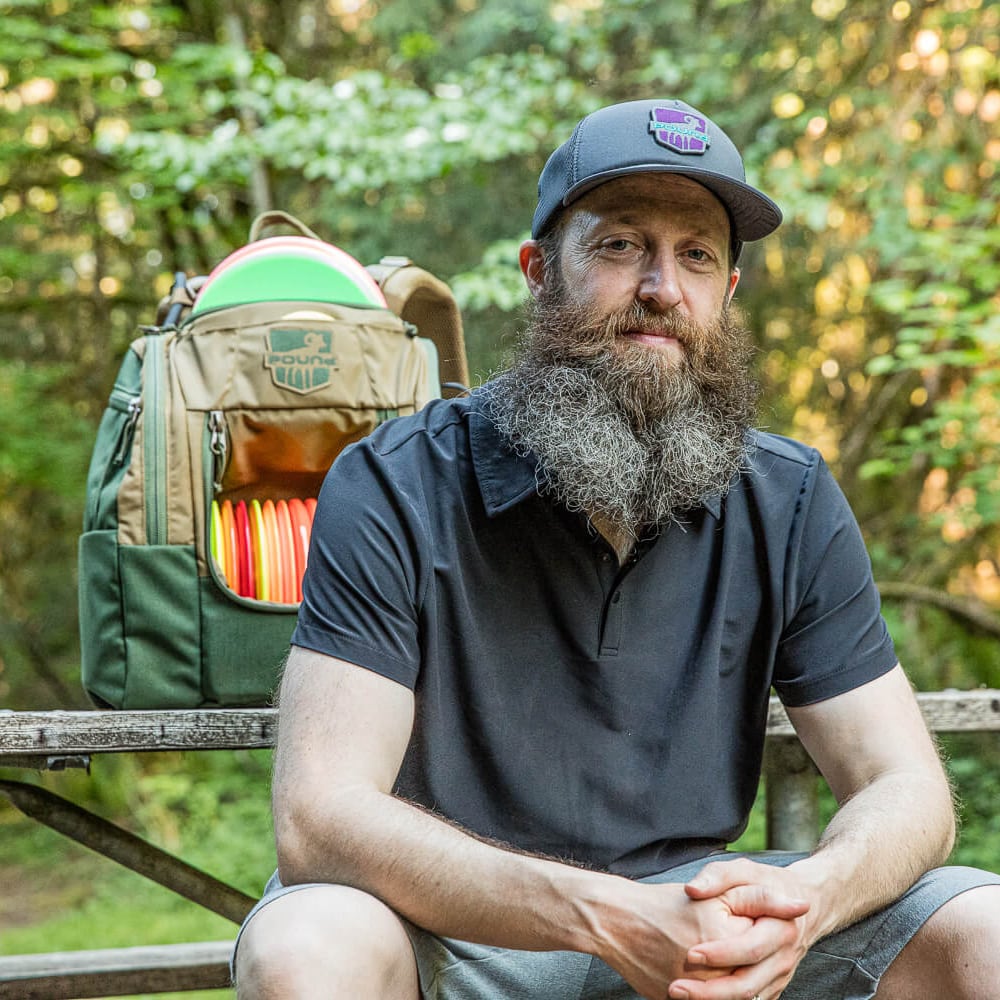 Pound's founder, Levi, sitting at a picnic table with a disc golf back behind him.