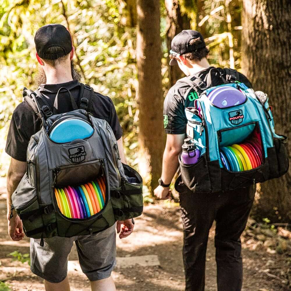 Two disc golfers walking down a trail while wearing Pound backpacks with several discs loaded into them.