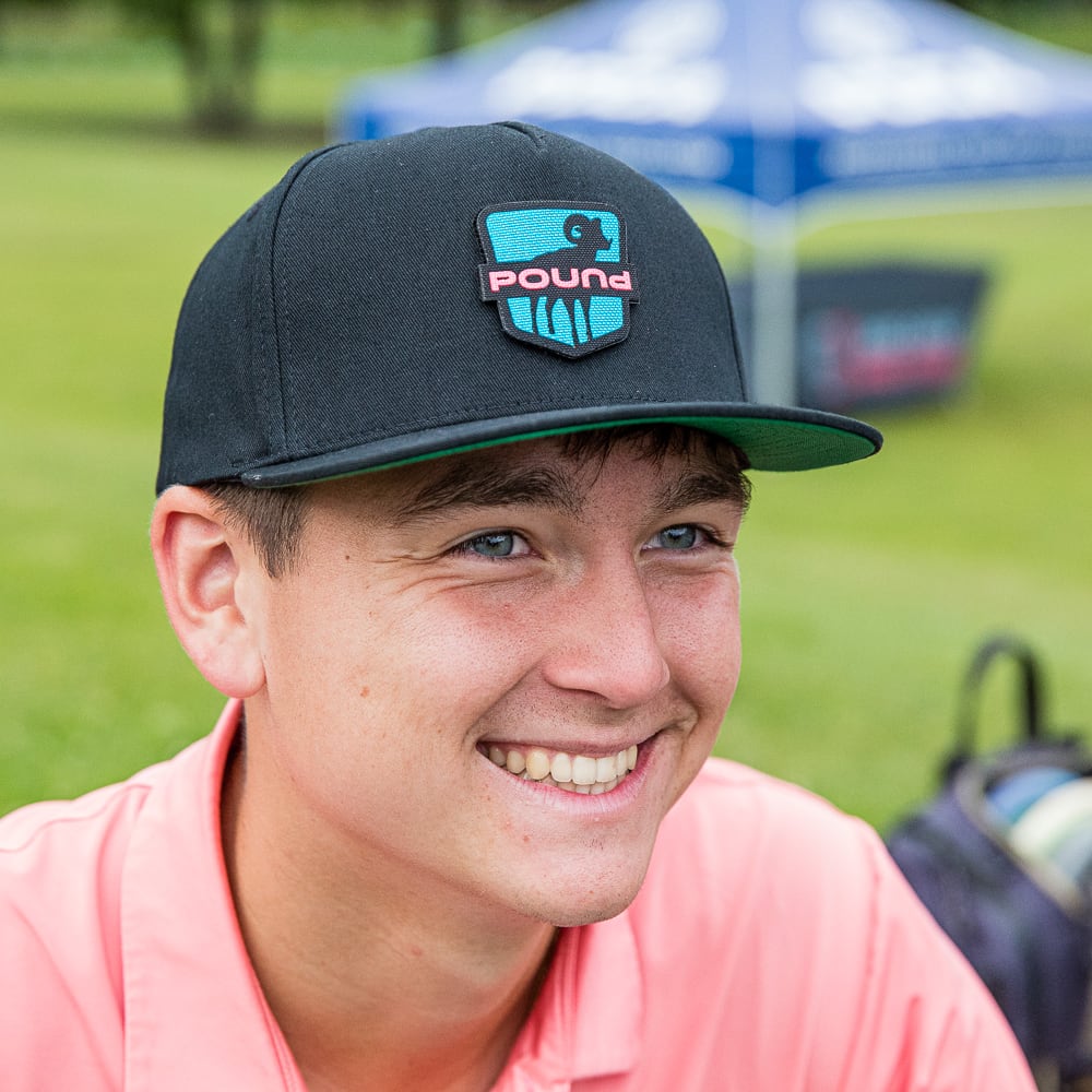 A disc golf athlete wearing a baseball cap featuring the Pound logo.